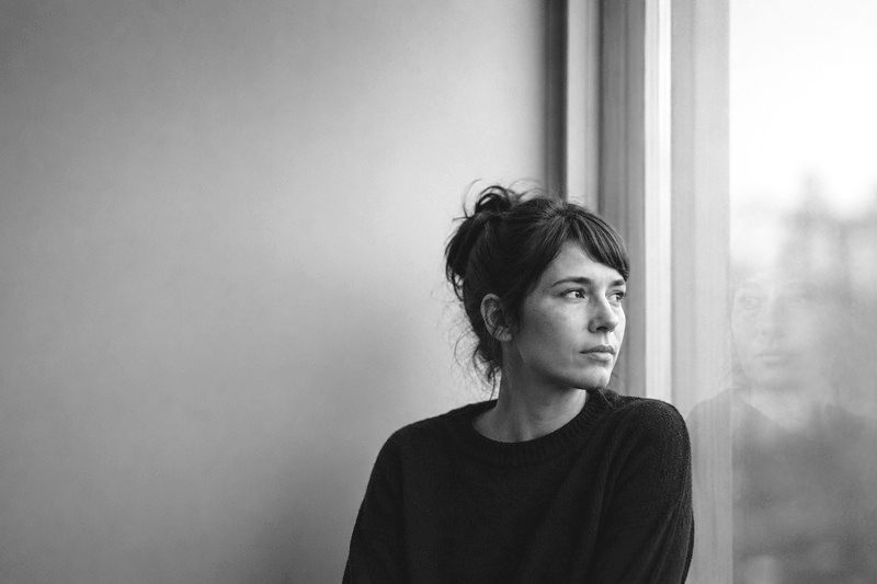 Portrait en noir et blanc d’une personne près d’une fenêtre, entourée d’un large espace vide.